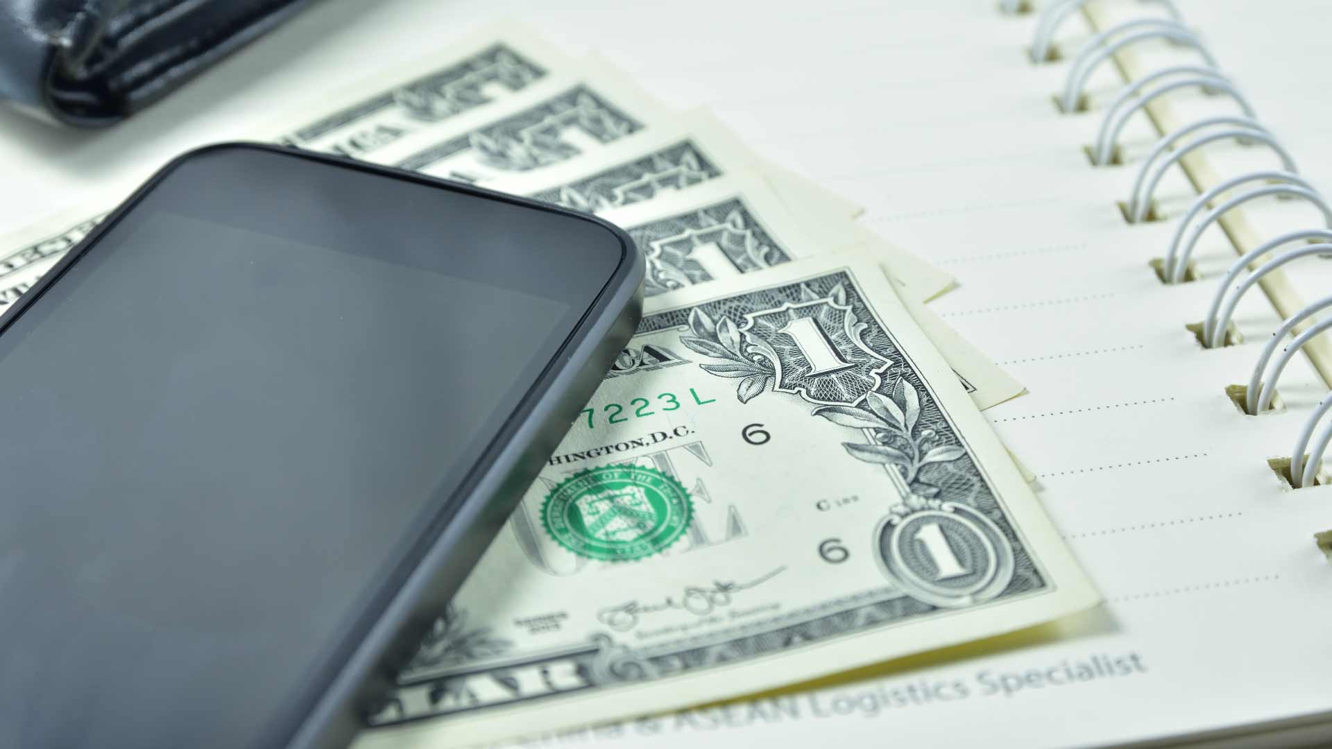 Celular sobre cédulas de dólar e caderno espiral, representando pagamentos digitais em Pix americano.
