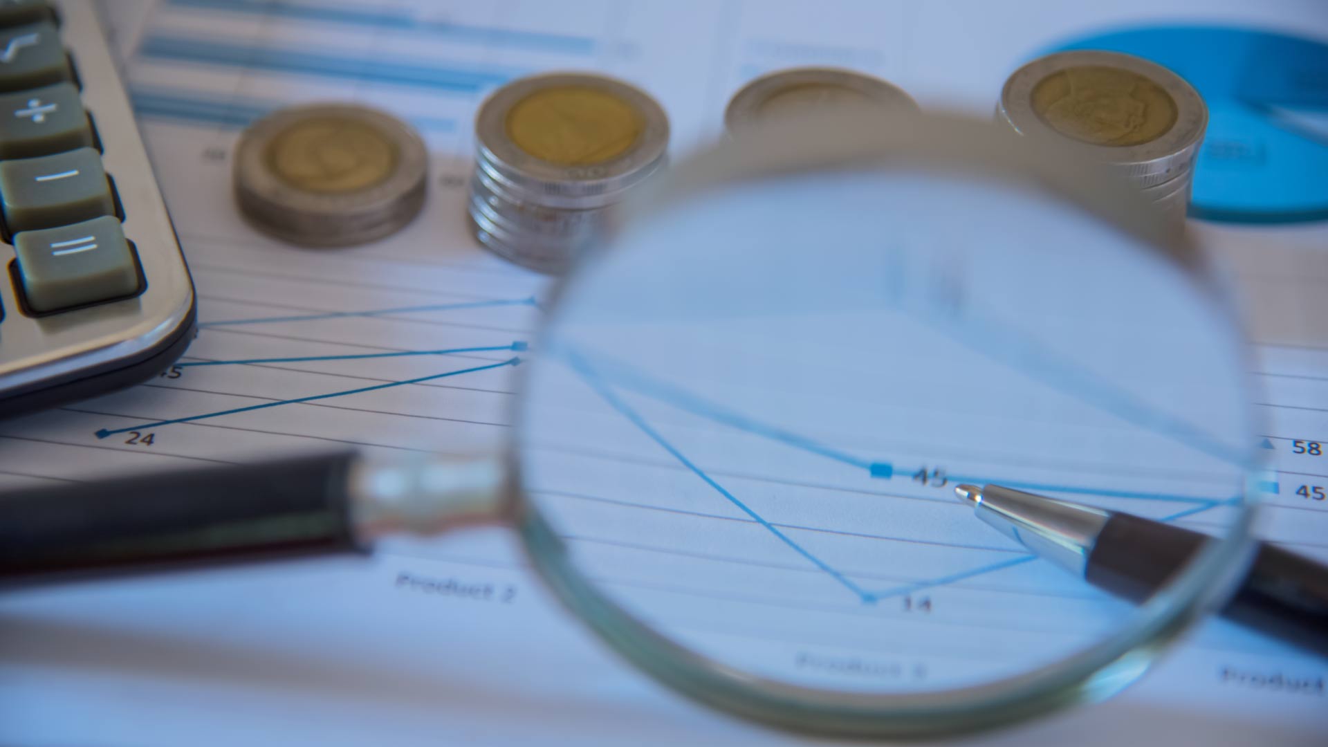 Lupa sobre gráfico financeiro com moedas e caneta ao fundo, simbolizando auditoria e compliance fiscal.