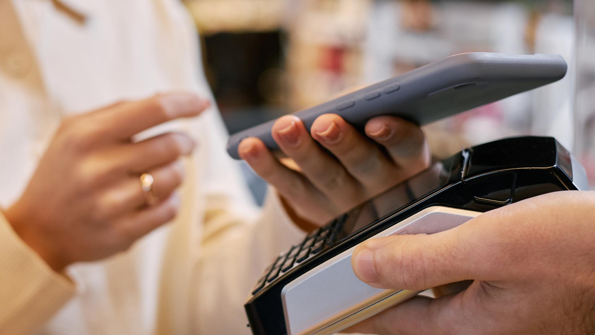 Close-up da mão de um cliente entregando um cartão de crédito ao lojista para pagamento em uma maquininha, representando a facilidade de acesso ao crédito no varejo e a agilidade nas transações comerciais.